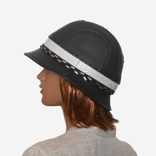 A woman's black leather hat with a small brim, decorative braid, and a warm lining, viewed from the side