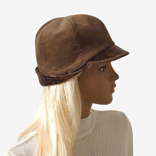 A brown corduroy cap with a small visor and a leather lapel, presented on a mannequin head.