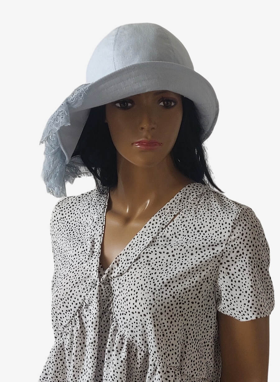 Front view of a romantic light blue linen summer hat with asymmetrical brim and delicate lace drapery