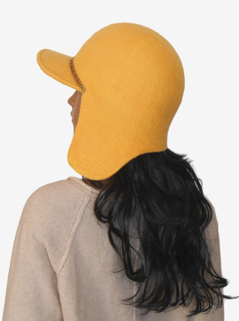 Side view of yellow felt trapper hat with ear flaps and visor