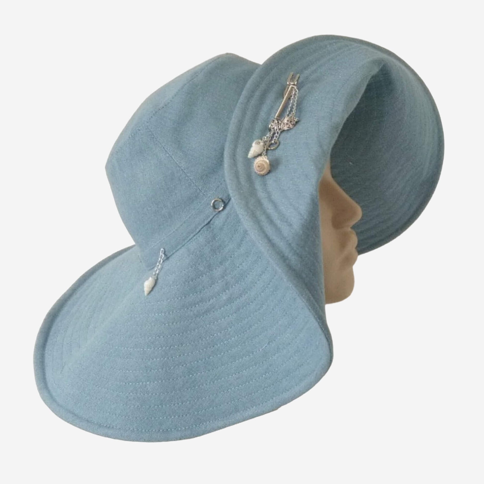 A blue denim wide-brimmed hat with decorative shells, rings, and chains displayed on a mannequin head.